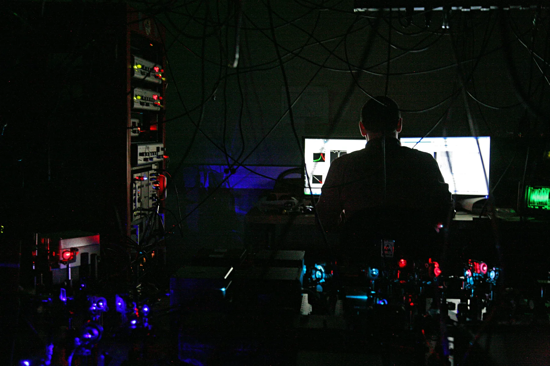 A researcher surrounded by illuminated optics and laboratory instruments